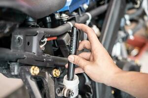 technicien chèques frein fluide dans moto avec frein fluide liquide testeur qualité vérifier stylo outil à garage, moto entretien et réparation concept photo