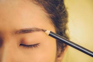 visage de beauté d'une femme asiatique en appliquant un crayon à sourcils sur la peau. photo