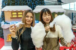 couple de Jeune Multi-éthnique femmes en mangeant de bonne humeur coton bonbons à une faire la fête. photo