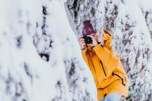 content fille photographe dans une Jaune veste prend des photos de hiver dans une neigeux parc