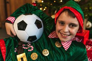 portrait de Jeune elfe avec costume et football Balle mensonge dans de face de une Noël arbre - Qatar 2022 football monde championnat concept photo