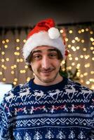 portrait de souriant Jeune homme portant rouge chapeau dans de face de une mur de Noël lumières photo