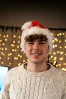 portrait de souriant Jeune homme portant rouge chapeau dans de face de une mur de Noël lumières photo