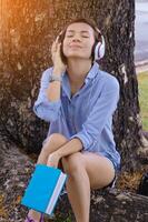 femme se détendre temps dans parc. elle écoute la musique en dessous de gros arbre. photo