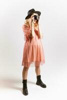 portrait de une mignonne fille photographe dans une chapeau posant avec une caméra dans sa mains dans le studio sur une blanc Contexte photo