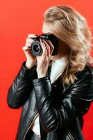 portrait de une magnifique fille photographe avec une caméra dans sa mains qui est photographié dans une photo studio sur une rouge Contexte