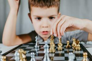 intelligent garçon apprend à jouer échecs par lui-même dans le sien pièce à Accueil photo