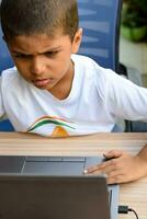 peu garçon séance à table en utilisant portable pour en ligne classe dans classe 1, enfant en train d'étudier sur portable de Accueil pour distance apprentissage en ligne éducation, école garçon les enfants mode de vie concept photo