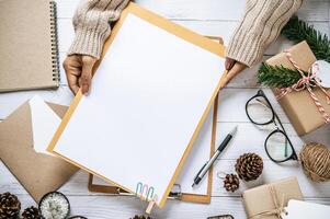 presse-papiers à main sur une table en bois blanc avec lunettes, stylo et pommes de pin séchées photo