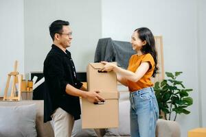 asiatique Jeune attrayant couple homme et femme utilisation tablette et téléphone intelligent en ligne achats meubles décorer maison avec carton paquet bouge toi dans Nouveau maison. Jeune marié asiatique en mouvement maison. photo