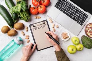 Mains féminines écrivant dans le plan de repas des mots du bloc-notes, vue de dessus à plat photo