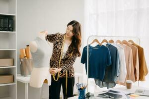 asiatique tailleur femme travail sur vêtements dans adaptation atelier. magnifique Jeune femelle mode designer sourire et après Succès dans moderne studio photo