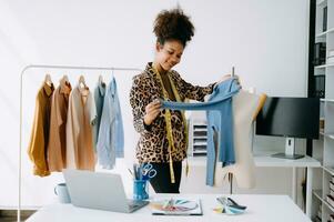 africain tailleur femme travail sur vêtements dans adaptation atelier. magnifique Jeune femelle mode designer sourire et après Succès dans studio photo