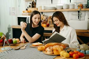 deux magnifique femme dans le cuisine dans un tablier, Frais des légumes sur le bureau, écrit vers le bas sa préféré recettes, vient en haut avec des idées pour vaisselle photo