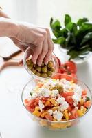 mains féminines faisant de la salade grecque ajoutant des olives au bol photo