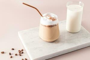 une grand verre avec une Chocolat boisson et Chocolat cales, une latté avec mousse sur une marbre blanc podium avec une cruche de lait. le parfait dessert. photo