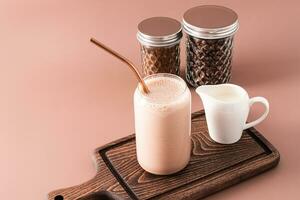 fraîchement fabriqué Milk-shake ou café avec Lait dans une moderne Bière en forme de boîte verre sur une en bois Coupe planche. de face voir. photo