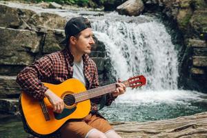 homme jouant de la guitare assis près d'une cascade