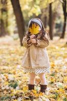 heureuse petite fille tenant une feuille d'érable jaune dans le parc en automne