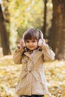 heureuse petite fille écoutant de la musique au casque dans le parc en automne. photo