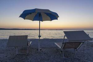 image de le le coucher du soleil sur le plage de le croate côtier ville de fazana avec Soleil fainéant et parasol photo