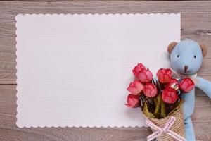 table en bois papier à lettre blanc ours bleu poupée tenant une fleur rose photo