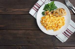 délicieux pilaf asiatique, riz cuit aux légumes et pilon de poulet sur une assiette. fond rustique en bois. copie espace vue de dessus photo