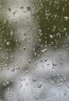 une photo de gouttes de pluie sur la vitre avec une vue floue des arbres verts en fleurs. image abstraite montrant des conditions météorologiques nuageuses et pluvieuses