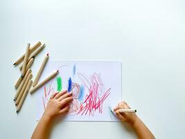 petit enfant dessine avec coloré des crayons sur papier sur blanc tableau. photo