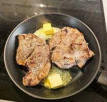 deux Haut aloyau du boeuf steaks dans une friture la poêle pendant cuisine avec deux pièces de beurre. Accueil nourriture concept. photo