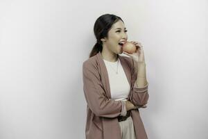 faim asiatique femme employé est content à propos le grignotage pomme, bouche mordre en bonne santé nourriture pour régime et biologique mode de vie, isolé par blanc Contexte photo