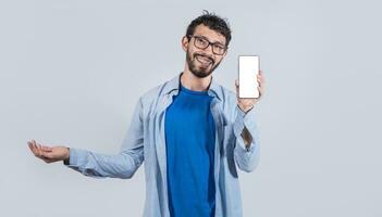 Beau homme souriant positif montrant mobile téléphone Vide écran avec un autre main paume ouvrir, excité content Masculin en portant téléphone intelligent photo