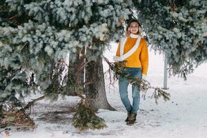 adolescent blond dans une Jaune chandail à l'extérieur dans l'hiver. une adolescent fille sur une marcher dans hiver vêtements dans une neigeux forêt photo