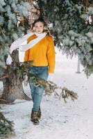 adolescent blond dans une Jaune chandail à l'extérieur dans l'hiver. une adolescent fille sur une marcher dans hiver vêtements dans une neigeux forêt photo