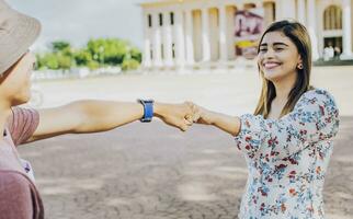 deux Jeune souriant adolescents cogner les poings dans le rue. proche en haut de gars et fille tremblement les poings dans le rue. une gars et fille tremblement mains sur le rue photo