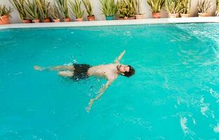 Jeune homme nager sur le sien retour dans une Hôtel bassin. concept de homme sur vacances profiter le piscine, homme sur vacances nager sur le sien retour dans une nager bassin photo