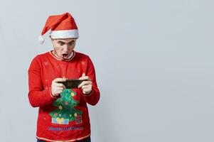 gars dans Noël chapeau à la recherche à une Noël promo sur téléphone. surpris homme en train de regarder une Noël promotion sur le téléphone, étonné homme dans Noël chapeau à la recherche à une Noël spécial des offres photo