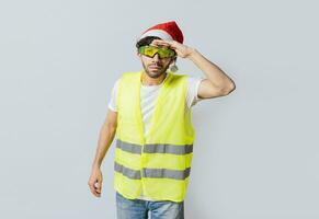 ingénieur dans Noël chapeau à la recherche à quelque chose dans le distance. ingénieur dans une gilet et Noël chapeau à la recherche dans le distance. constructeur homme dans une gilet et Noël chapeau à la recherche dans le distance photo