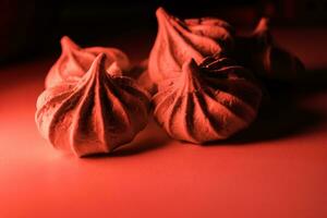 quatre Meringue biscuits dans rouge lumière sur une foncé Contexte. photo