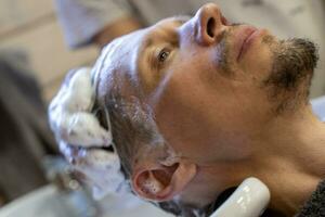 homme lavages le sien cheveux tandis que visite une coiffeur photo