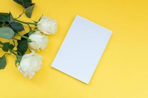 Haut vue de une Jaune table avec une maquette de Vide des cahiers avec une bouquet de des roses sur le côté. photo