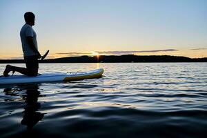 une homme sur une pagayer planche dans le des rayons de Soleil. photo