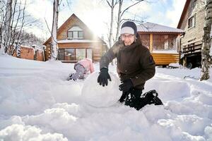 une famille construit une bonhomme de neige en dehors de neige dans le Cour dans l'hiver. photo