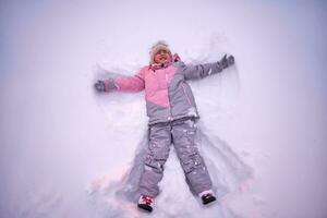 une fille fait du une neige ange dans blanc neige dans l'hiver. photo