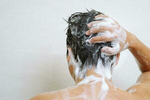 une homme est la lessive le sien cheveux avec shampooing photo