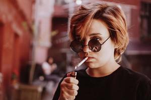 Fille aux cheveux roux courts et lunettes de soleil miroir fumant une cigarette