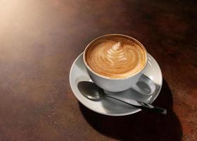 tasse d'art latte chaud dans la lumière de l'après-midi sur une table en bois photo