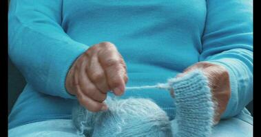 une femme avec tricot dans sa mains. le mains de un vieux femme à travaux d'aiguille. une femme dans bleu dissout une de laine foulard. photo