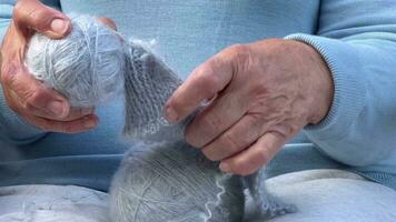 une femme avec tricot dans sa mains. le mains de un vieux femme à travaux d'aiguille. une femme dans bleu dissout une de laine foulard. photo