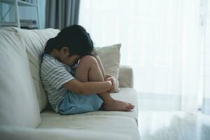 asiatique enfant fille dérangé solitaire intimidé peu séance étreindre votre les genoux sur le canapé canapé dans vivant pièce à Accueil se sent abandonné abusé, triste seul, charité adoption concept. photo